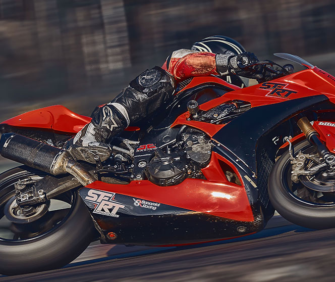 A motorcycle racer in full protective gear leans into a sharp turn on a red and black sportbike, speeding along a racetrack with a blurred background.