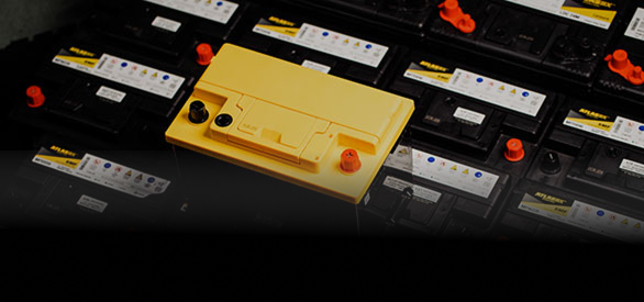 Multiple automotive batteries are displayed, with one distinctive yellow battery prominently placed on top of the black ones.