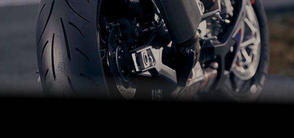 Close-up view of the rear wheel and suspension system of a modern sport motorcycle parked on an asphalt road.